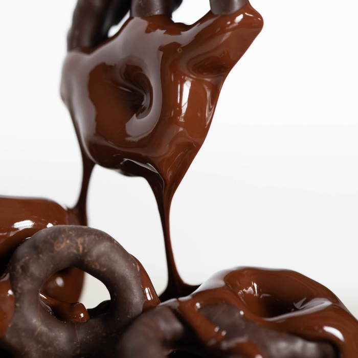 Dark chocolate dripping off a chocolate covered pretzels onto a pile of chocolate covered pretzels on a white background