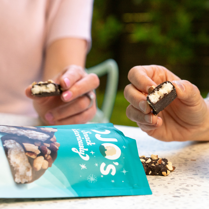 Two hands holding coconut filled ark chocolate bars with a blue package that reads "JOJOs Snack Victoriously"