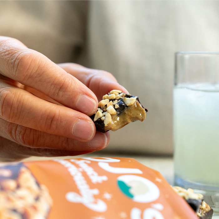 Hand holding a dark chocolate peanut butter bar bit in half with a glass of lemonade in the background