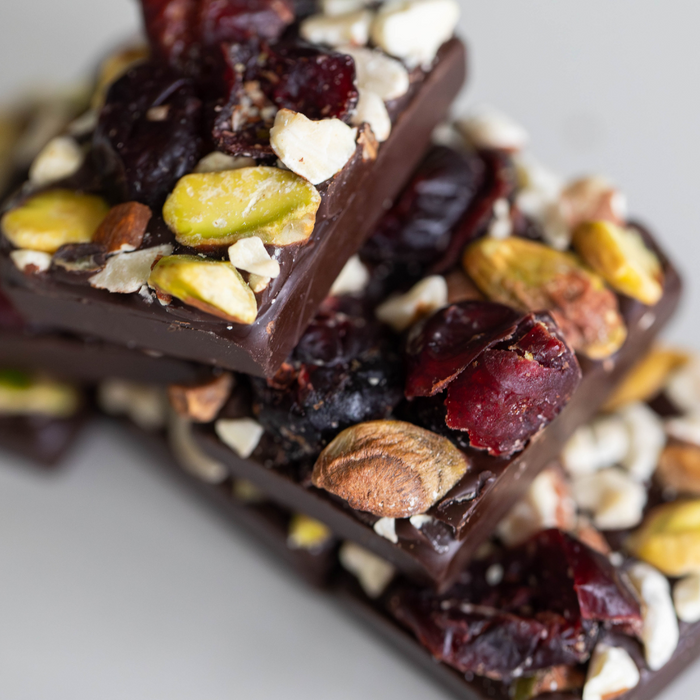 Stack of dark chocolate bars with cranberries, pistachios and almonds on top. White background