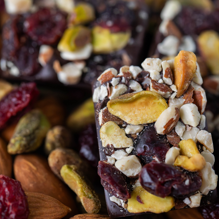 Close up of a dark chocolate bar topped with cranberries pistachios and almonds. Background is cranberries pistachios and almonds