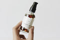 Hand holding a bottle of body oil with a Karomni label against a light background