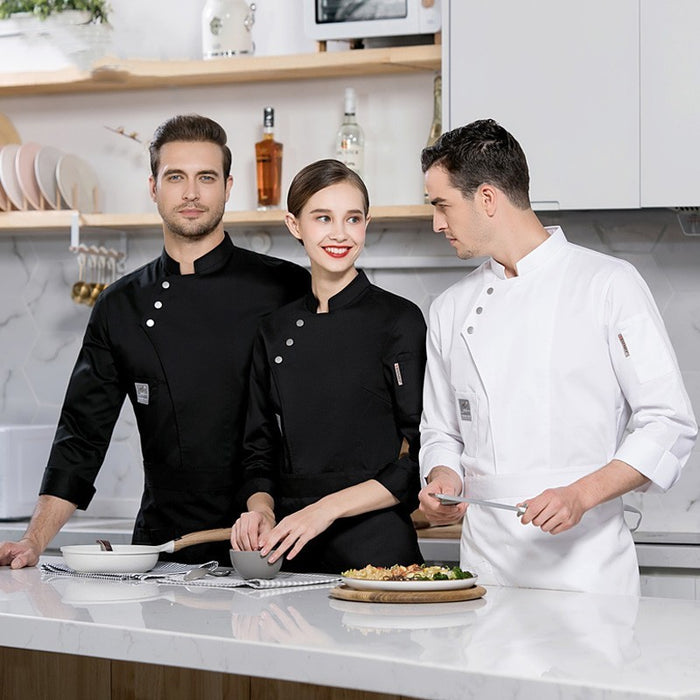 Two adults, one male and one female, wearing long sleeve chef uniforms in a kitchen setting. The male chef is in a white uniform, and the female chef is in a black uniform.