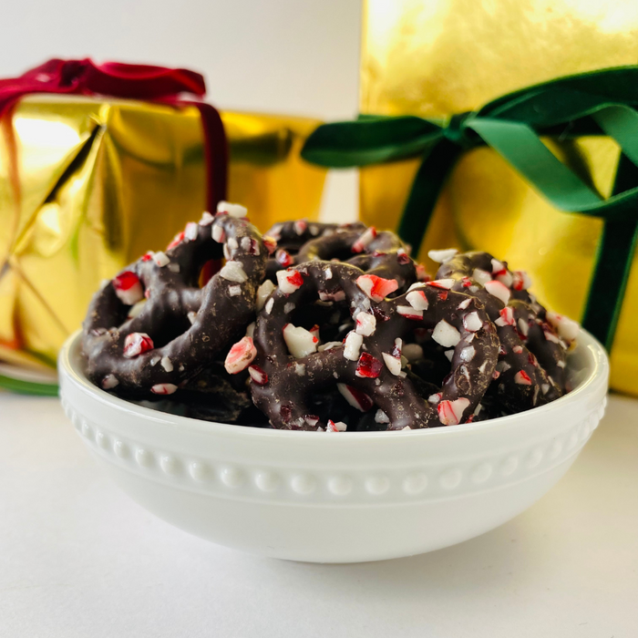White bowl containing dark chocolate coated pretzels with peppermint pieces and presents in the background