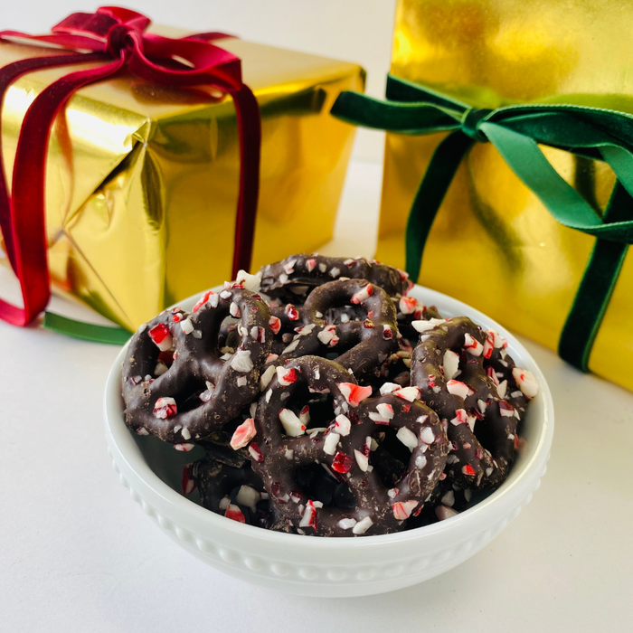 White bowl containing dark chocolate coated pretzels and peppermint pieces with presents in the background