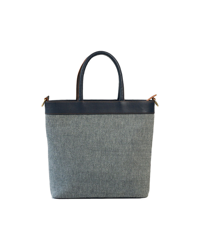 A structured tote bag with a textured gray woven body, a black leather top band and handles, and small gold-tone hardware on the sides, shown against a plain white background.