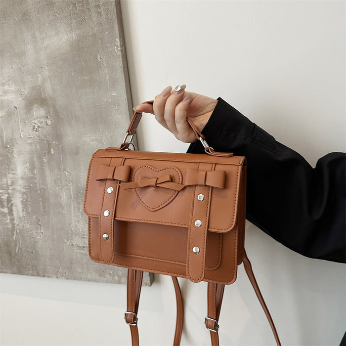 A person holding a brown, vintage-style faux leather shoulder bag with a structured design and a heart detail on the front.